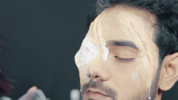 Make up artist coloring prosthetic insert on man's face and making Halloween mask