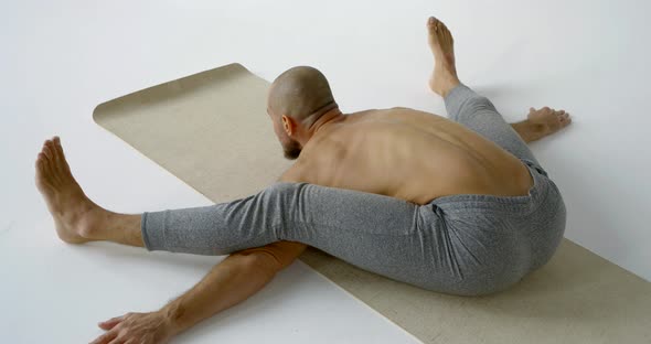 Male Athlete Is Stretching Body, Lying By Torso on Floor and Putting Legs on Hands