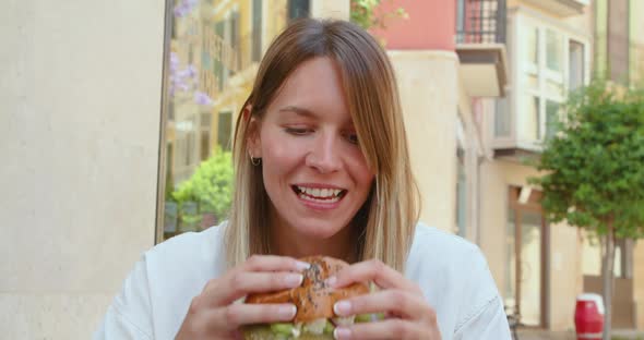 Laughing woman having burger while enjoying lunch with friend