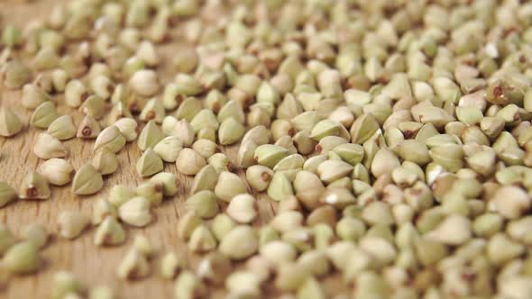 A wholesome uncooked green buckwheat grain falls onto a wooden surface