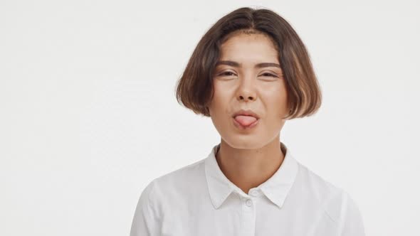 Young Beautiful Brunette East Asian Female in Shirt Showing Tongue Making Faces Smiling on White