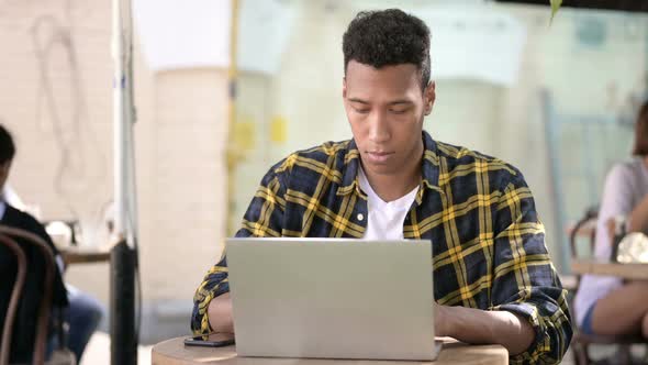 Young African Man Working on Laptop, Outdoor Cafe