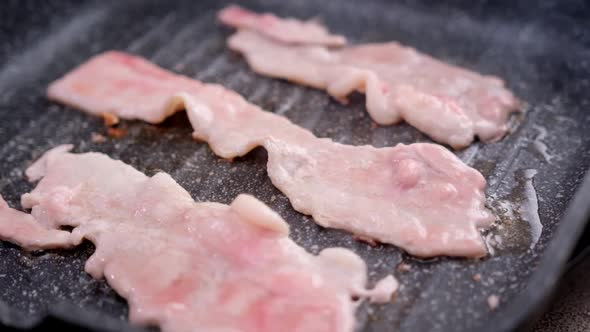 Cooking Pieces of Flavorful Sliced Organic Bacon Fried in Grill Pan