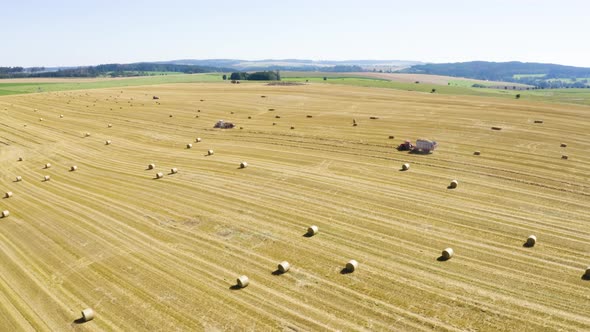 Aerial Drone Shot  a Field with Tractors and Hay Bales in a Rural Area on a Sunny Day
