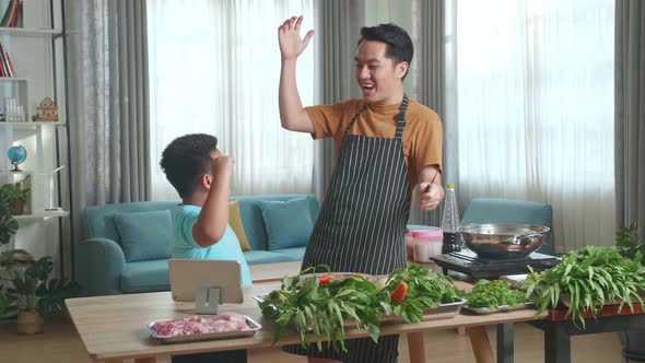 Asian Man Father Giving High Five To Happy Little Child Son While Cooking At Home