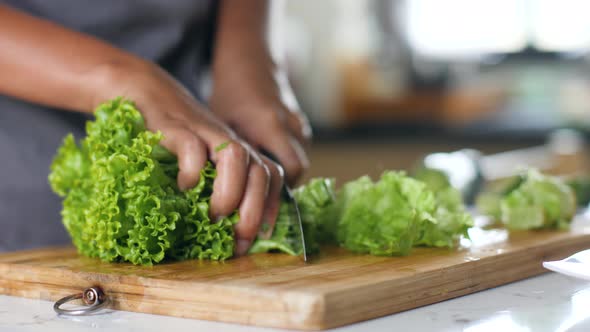 Woman's Hands Chopping the Fresh Green Lettuce on Chopping Board in the Kitchen.