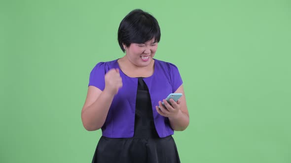 Happy Young Overweight Asian Woman Using Phone and Getting Good News