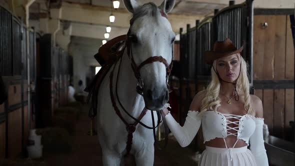 Beautiful Horsewoman is Leading White Horse From Barn to Walk Portrait Shot in Stable