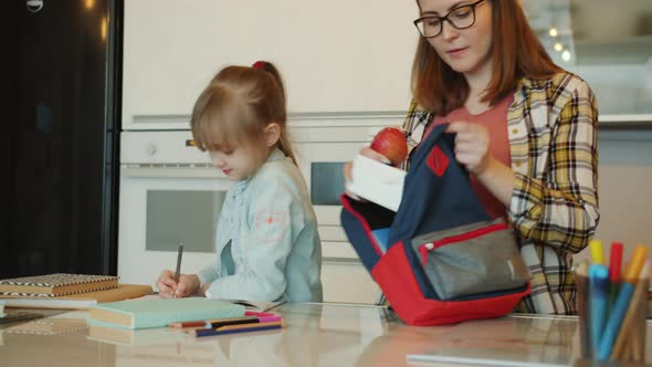 Pregnant Mother Giving Lunch Box To Cute Daughter Saying Good-bye Before School