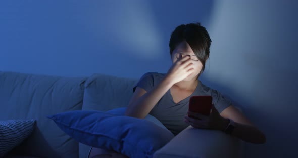 Woman use of mobile phone at night and sit on sofa at home