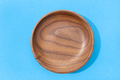 Empty round wooden plate or bowl isolated on blue background. Walnut wood. Top view - PhotoDune Item for Sale