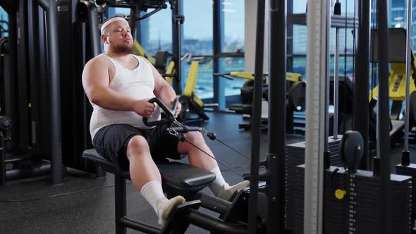 Fat Burning Overweight Funny Man Lifting Blocks on Rowing Machine Training on Block Device and Gym