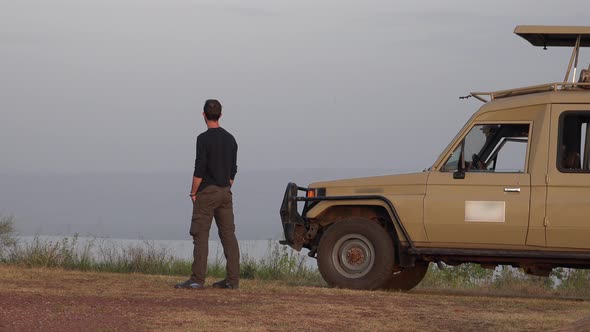 A Male Tourist Watches Africa Landscape by Standing in Front of a Safari Vehicle