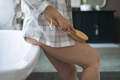 Adult woman in pajama doing body massage with dry wooden brush with natural bristles in bathroom  - PhotoDune Item for Sale