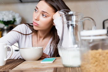 of sad girl near bowl, jug, cup and smartphone with
