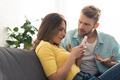 Depended woman using smartphone near angry boyfriend on couch - PhotoDune Item for Sale
