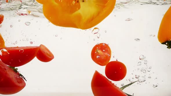 Peppers and Tomatoes Plop Into Water with Splashes and Bubbles, Slow Motion Close-up
