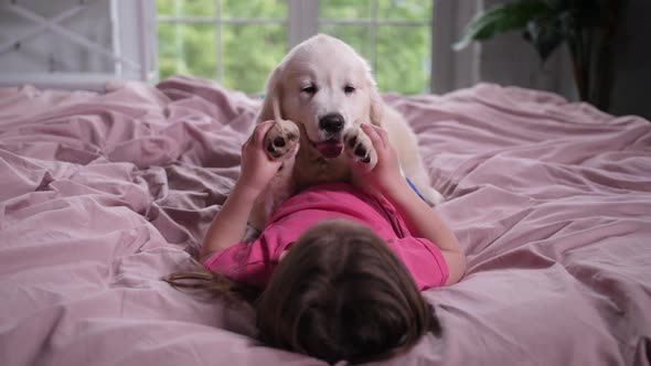 Little Girl Playing with Puppy Pet Lying on Bed