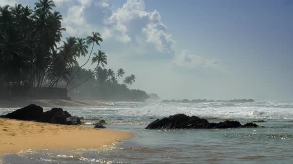 Blue Ocean Waves Roll on Yellow Sandy Beach with Brown Rocks