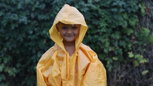A Little Boy Stands in the Rain in a Raincoat