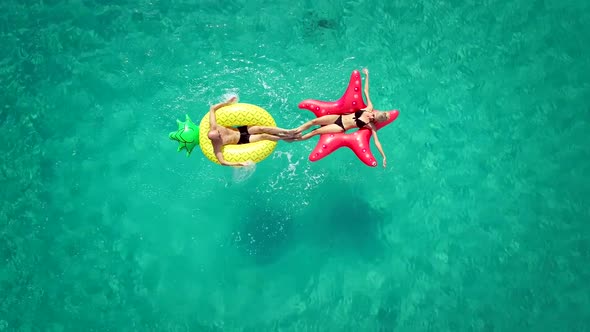 Aerial view of man and woman splashing each other on inflatable mattresses in sea.