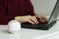 A man checking baseball stats on laptop. White leather ball on the table. Betting, gambling concept. - PhotoDune Item for Sale