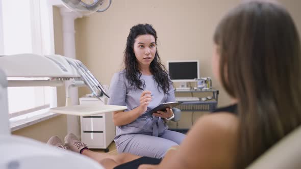 Portrait of Young Beautiful Female Dentist Talking in Slow Motion with Teenage Patient Sitting in