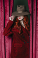 Stylish redhead woman in hat peek through the viva magenta color curtains - PhotoDune Item for Sale
