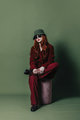Stylish woman in sunglasses, hat and red suit sits on green background - PhotoDune Item for Sale