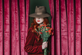 Stylish redhead woman in hat with carnations peek through the viva magenta color curtains - PhotoDune Item for Sale