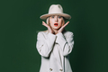Suprised stylish blond hair woman in white blazer and hat on green background - PhotoDune Item for Sale