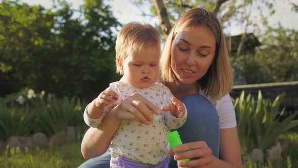 A smiling young mother hugs her little daughter, and blows soap bubbles