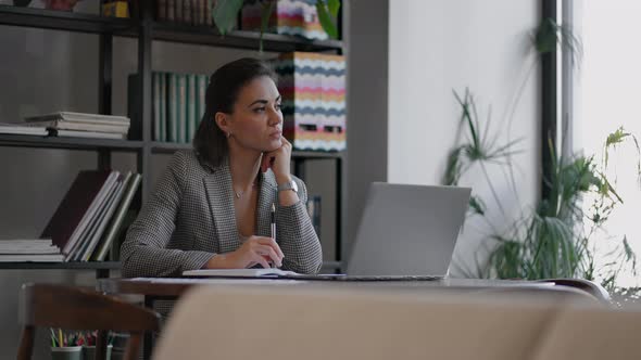 Arabian Hispanic Woman Working Financial Paperwork Seated at Workplace Using Laptop Looks