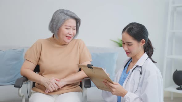 Asian young caregiver take care senior woman on wheelchair in house.