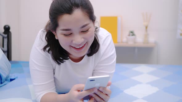 Asian woman looking and touching smartphone relax enjoy and smile with online social media in bedroo