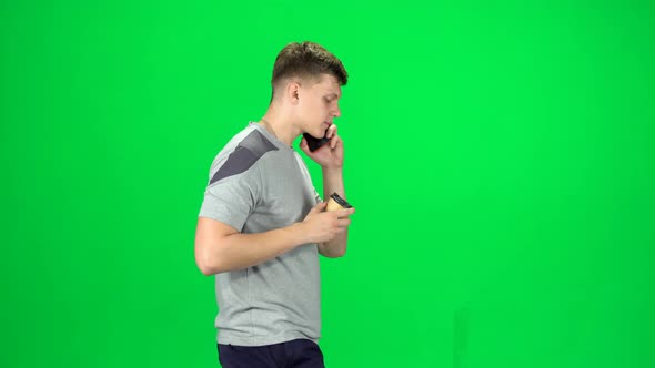 Young Man Walking Talking on the Phone and Drinking Coffee. Chroma Key. Side View