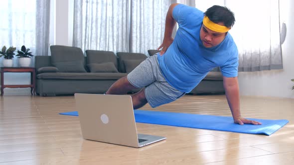 Fat Man Doing Exercises At Home While Watching Online Tutorial On Laptop