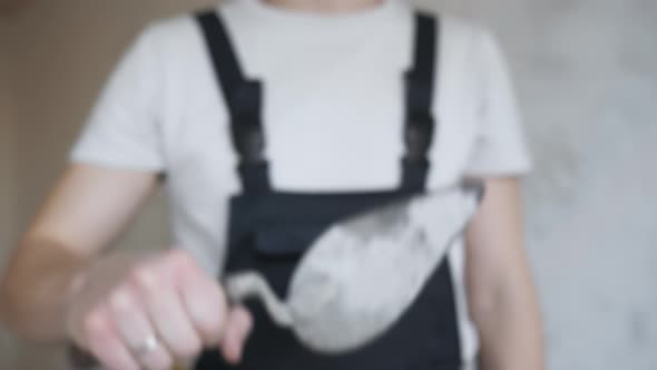 A Construction Worker in Overalls Shows a Construction Trowel To the Camera