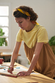 Vertical image of young craftswoman in yellow t-shirt bending over workplace - PhotoDune Item for Sale