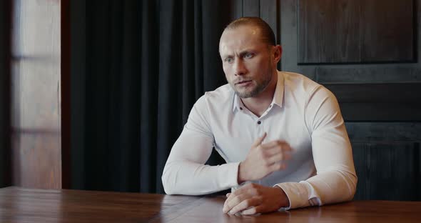 Man Seated at a Table Clasping His Chest in Pain