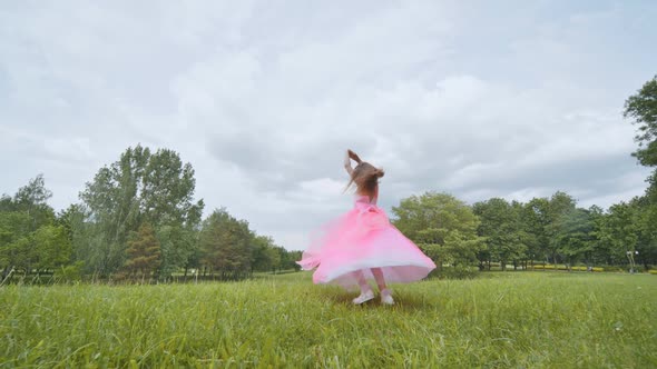 A Girl in a Pink Princess Dress is Spinning in the Park