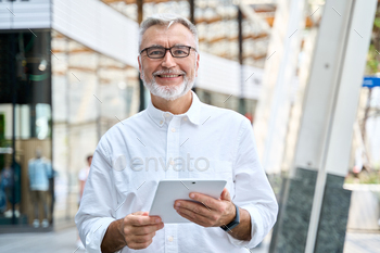 Old senior professional business man using digital tablet standing outdoors.