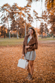 Portrait of a girl, posing for the camera, holding a purse, being at the park during the autumn. - PhotoDune Item for Sale
