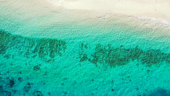 Vivid colors of turquoise sea water over beautiful patterns of coral reefs and rocks, near white san