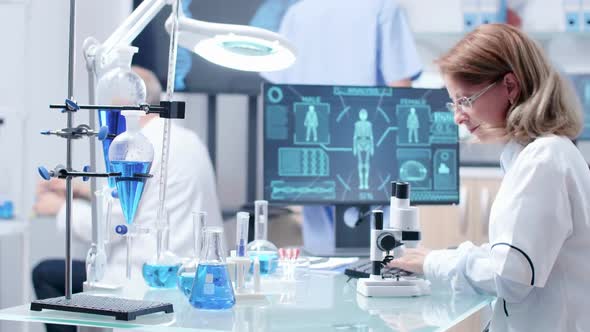 Female Researcher Typing on Computer Keyboard and Looking in a Microscope