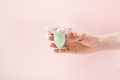 Menstrual cup with small white flowers in a female hand against a pink background - PhotoDune Item for Sale