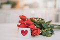 Bouquet of red roses and small card with painted red heart on white table - PhotoDune Item for Sale