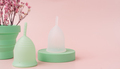 Menstrual cups on green podium next to red dry flowers in power case against pink background - PhotoDune Item for Sale