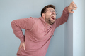 European man is suffering from severe back pain, he is screaming while holding hand against the wall - PhotoDune Item for Sale