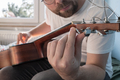 Acoustic guitar tuning. Focused man repairs a stringed musical instrument, indoors. - PhotoDune Item for Sale